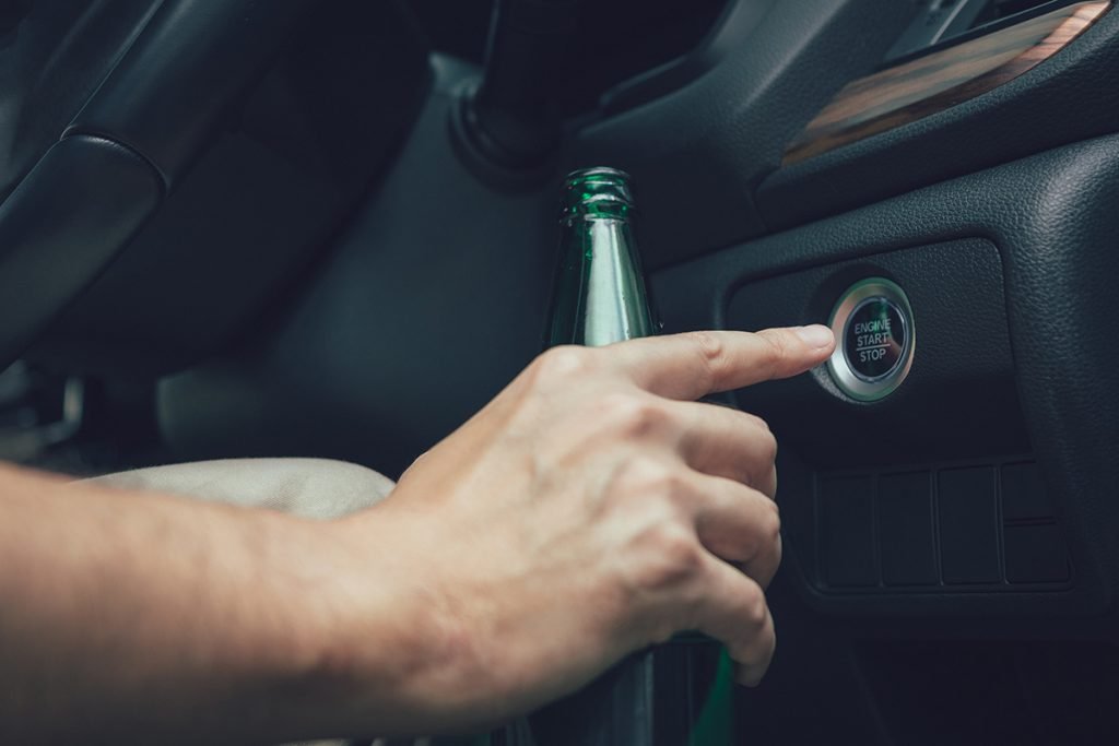 A driver engaging a vehicle ignition while holding a beer bottle