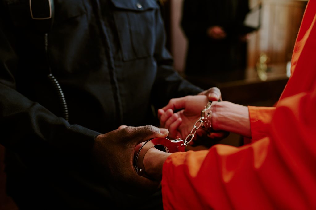 A young man in handcuffs standing in front of an officer